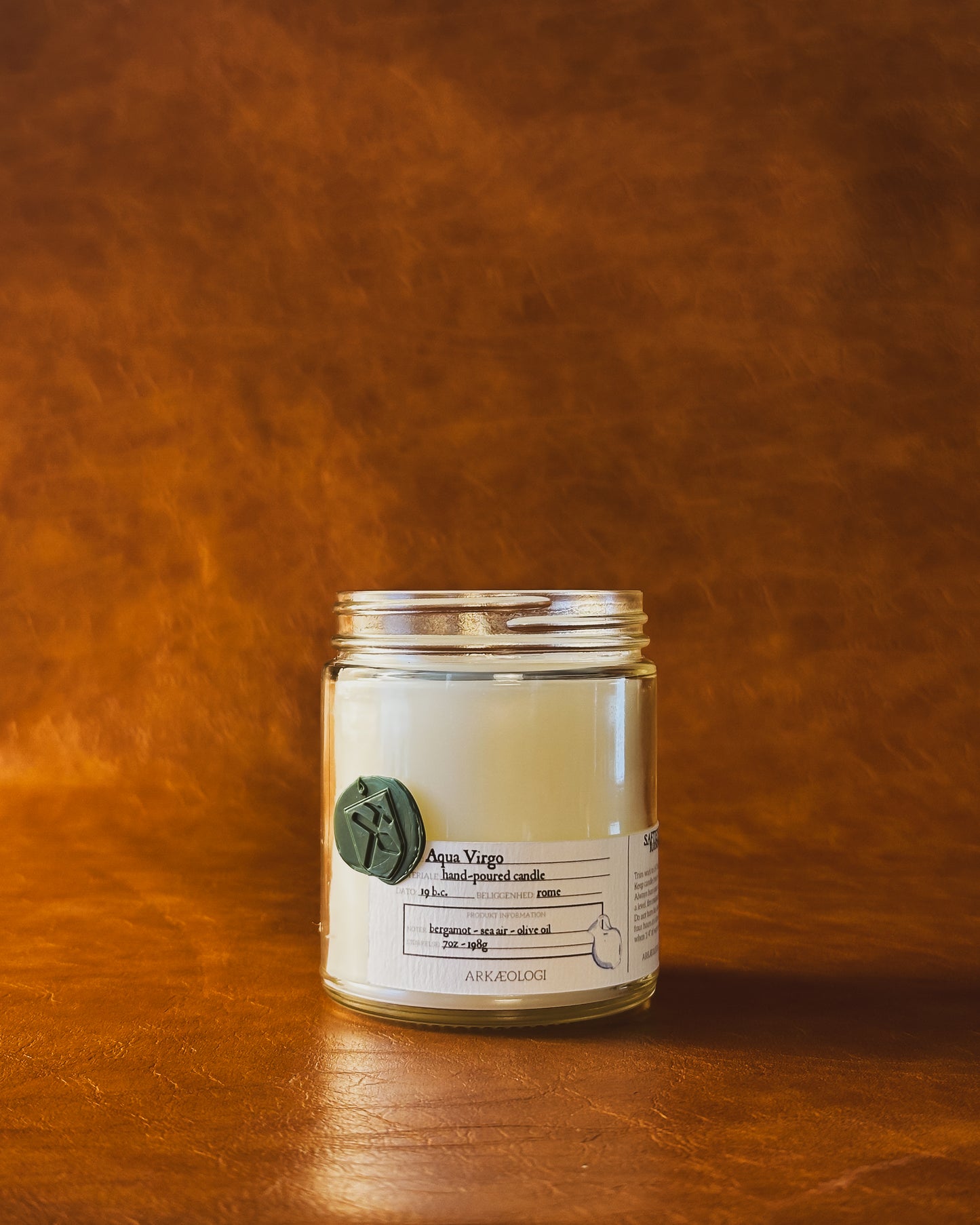 Aqua Virgo candle jar with green wax seal and white label inspired by artifact tag, no lid on leather background