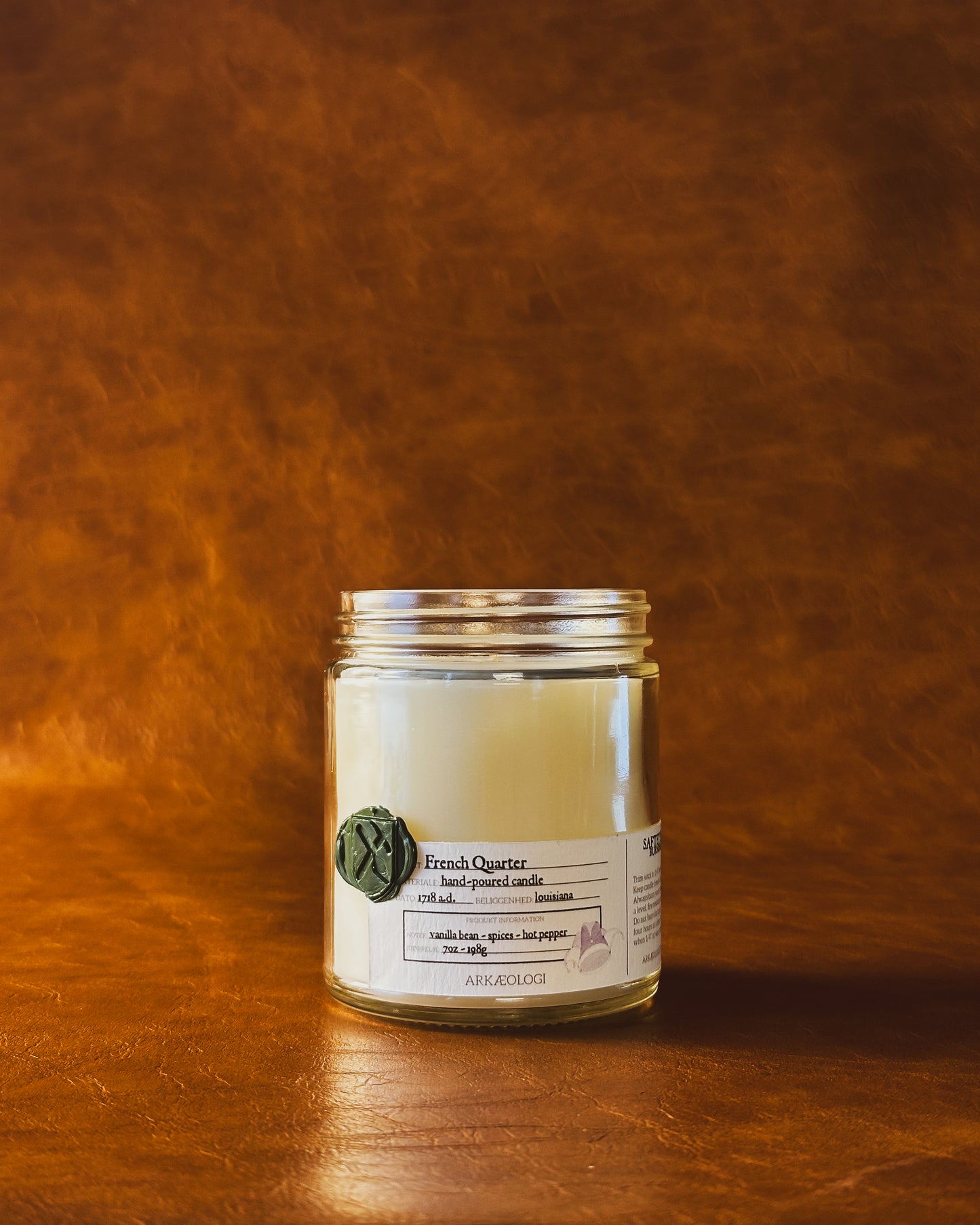 French Quarter candle jar with green wax seal and white label inspired by artifact tag, no lid on leather background