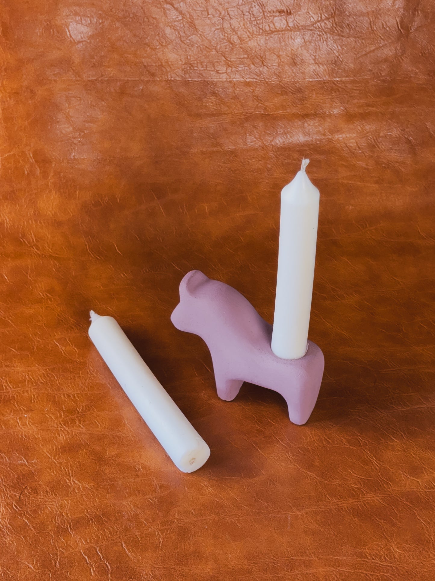 Pink concrete Dala horse candle holder with two taper candles on vintage newspaper background.