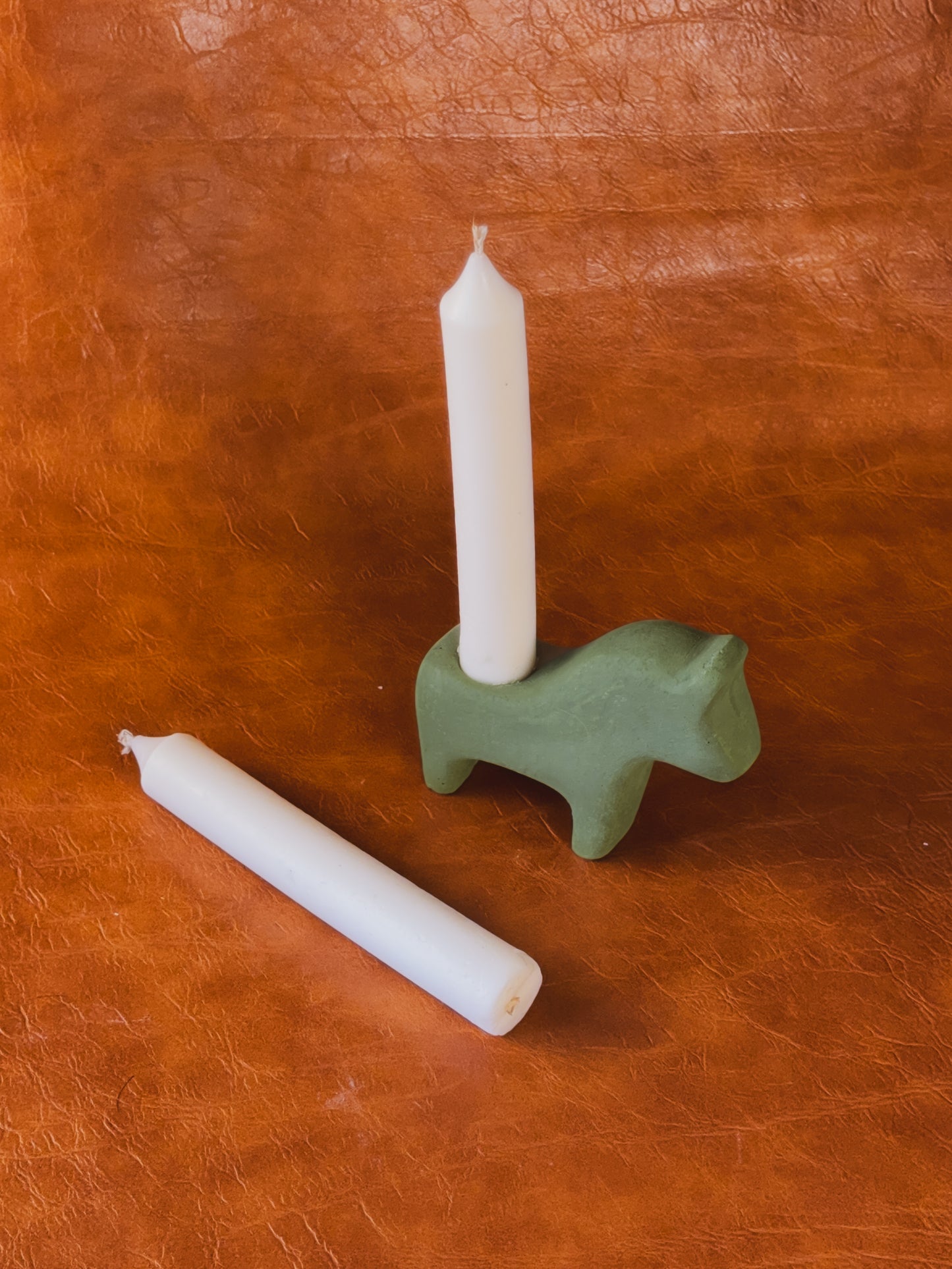 Green concrete Dala horse candle holder with two taper candles on vintage newspaper background.