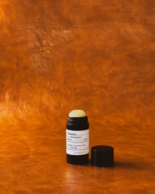Poseidon Solid Fragrance in black tube on leather background.