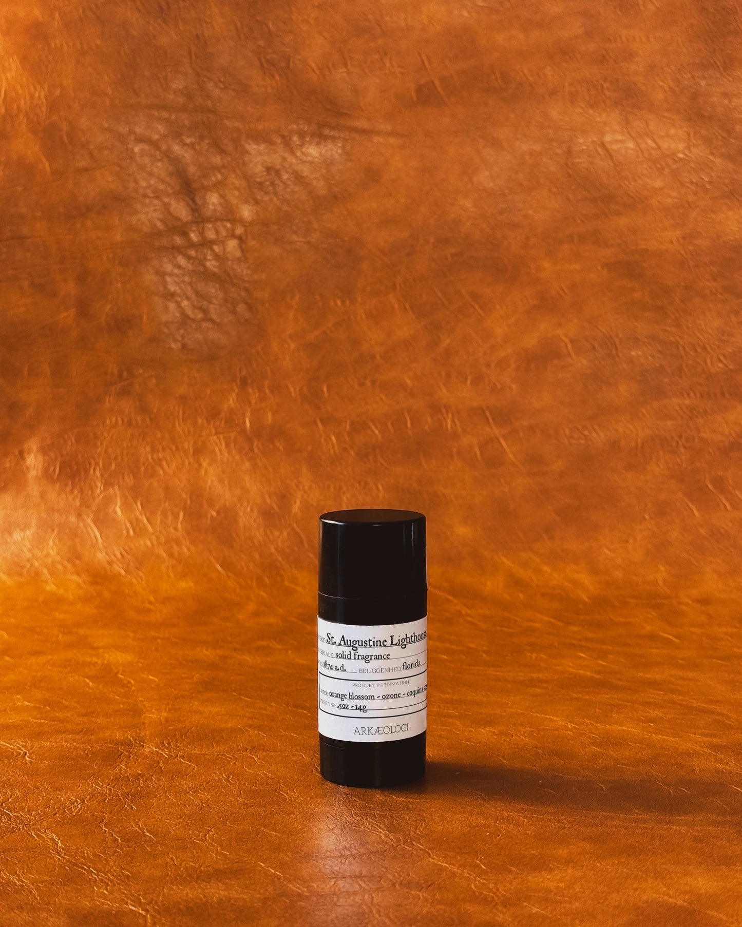 Saint Augustine Lighthouse Solid Fragrance in black tube on leather background.