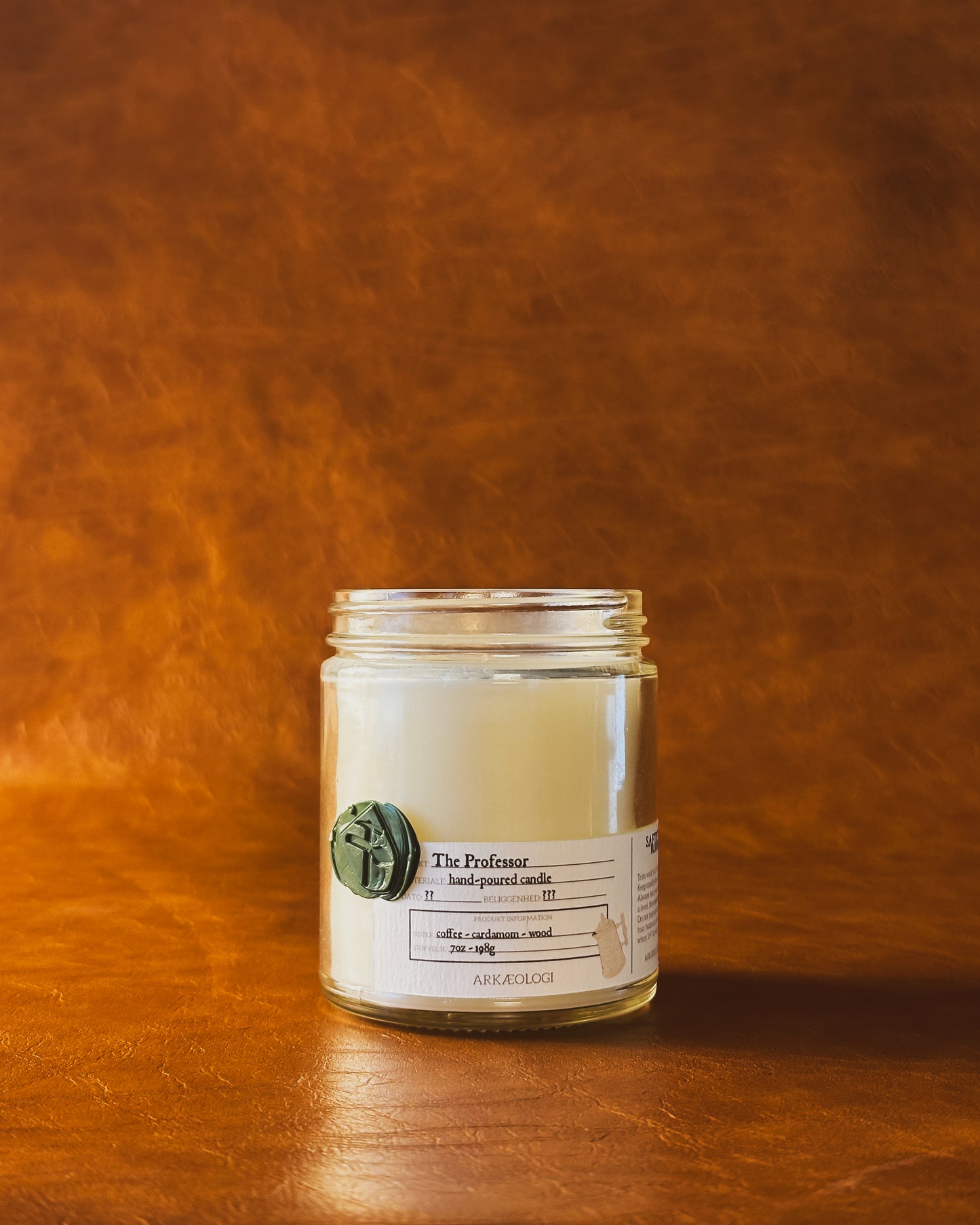 The Professor candle jar with green wax seal and white label inspired by artifact tag, no lid on leather background