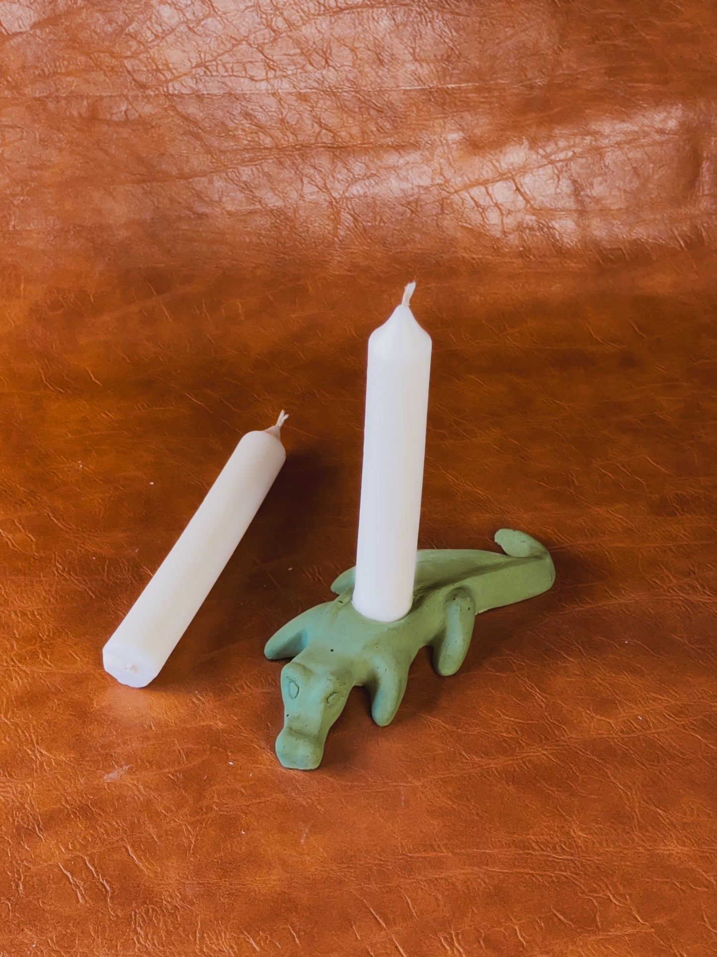 Green alligator candle holder with two taper candles on brown leather background.