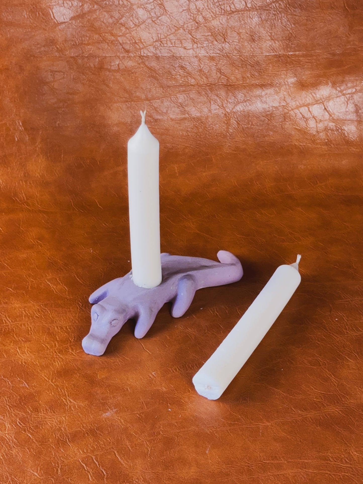 Purple alligator candle holder with two taper candles on brown leather background.
