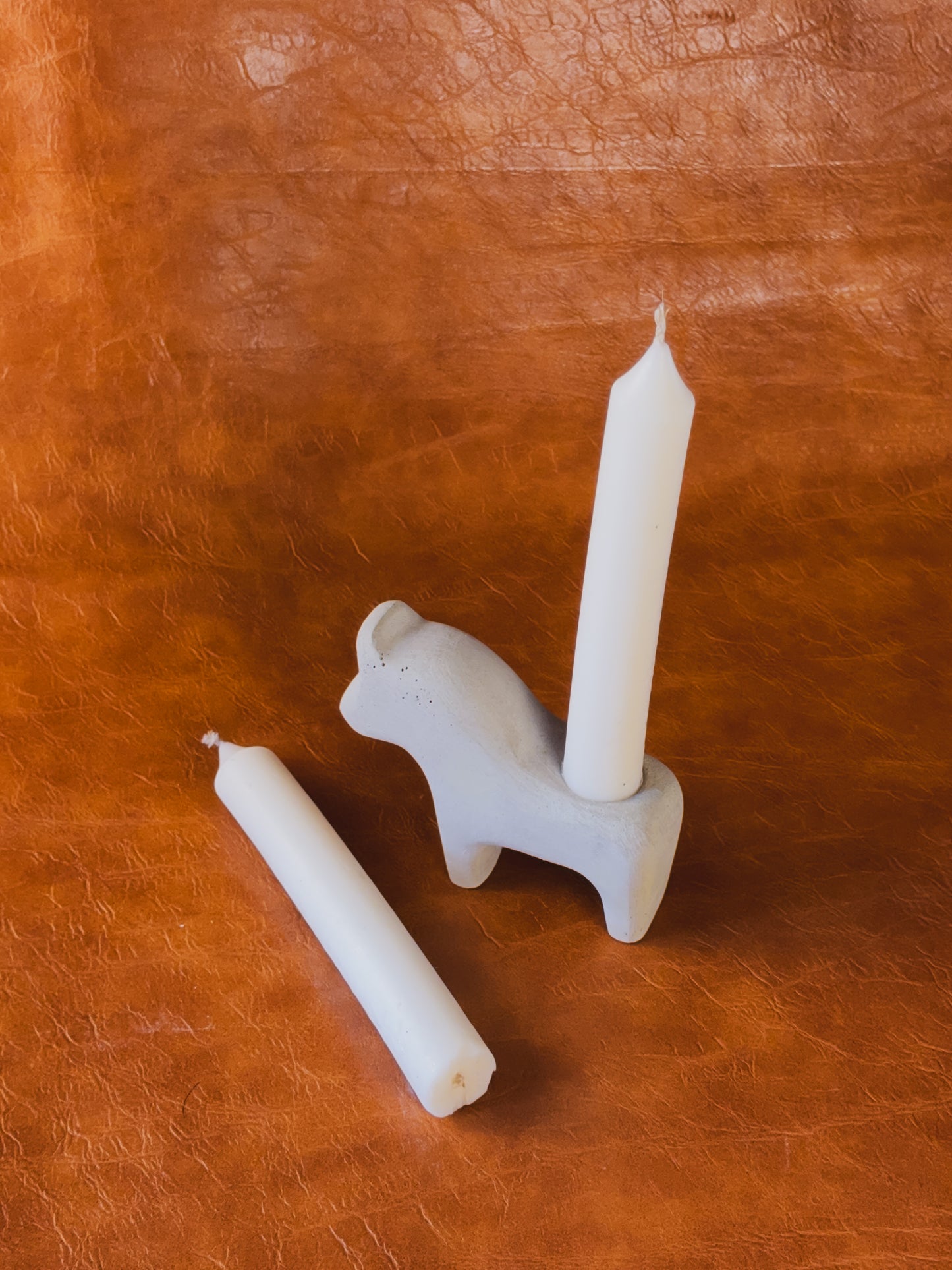 White concrete Dala horse candle holder with two taper candles on vintage newspaper background.