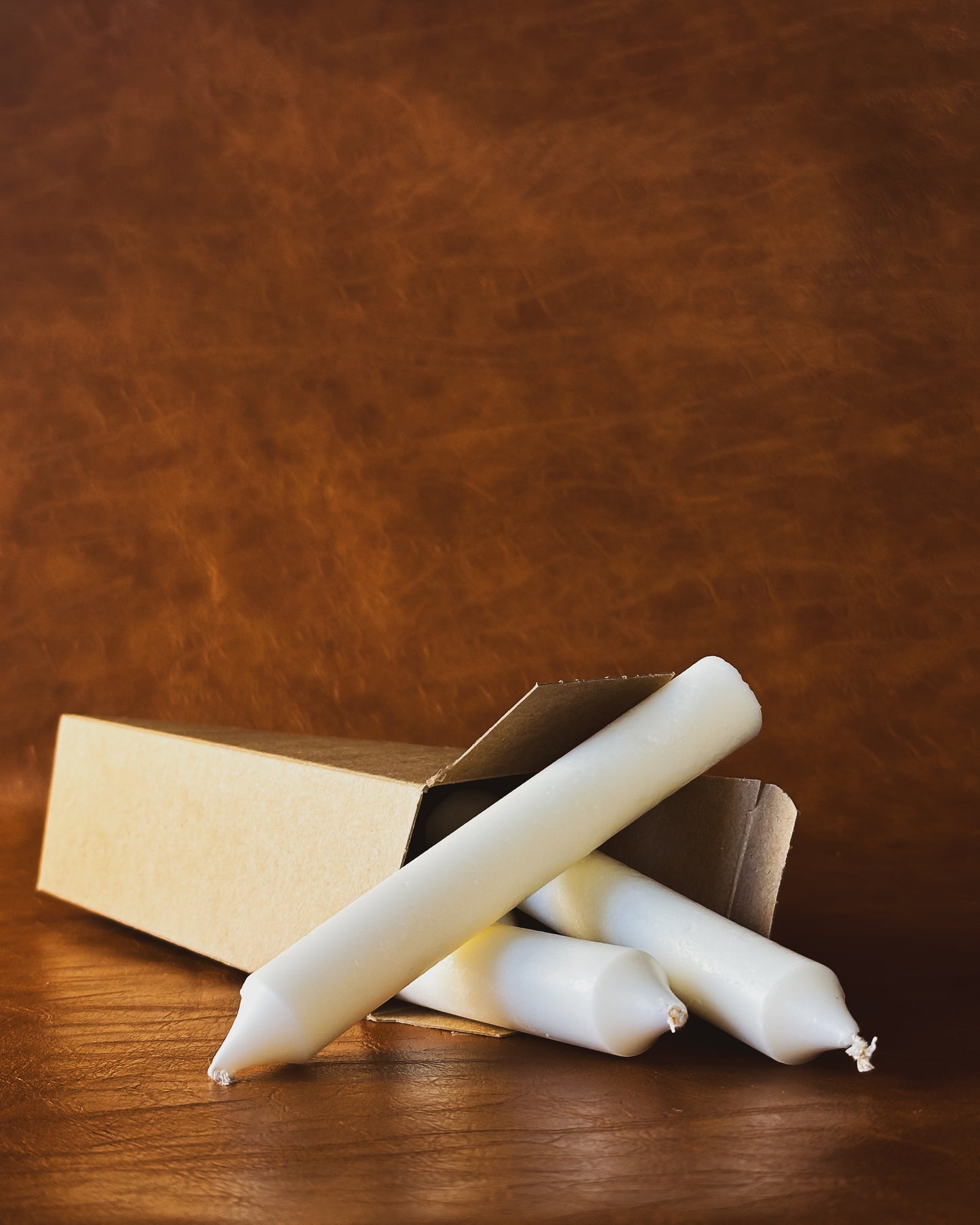 Four taper candle in Kraft paper box on brown leather background