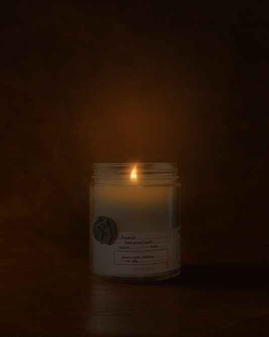 Lit Amande in clear jar with green wax seal and white label inspired by artifact tag on leather background