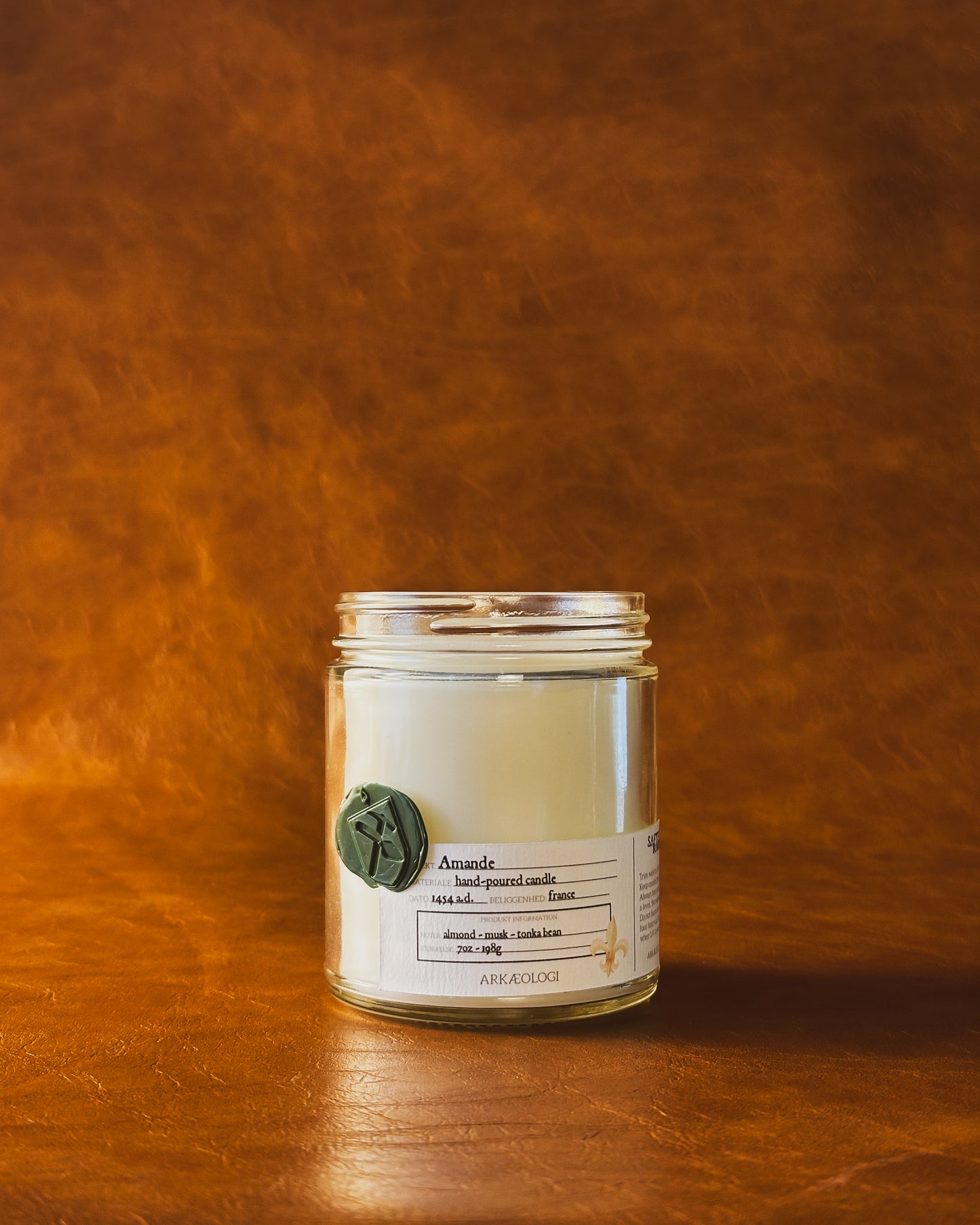 Amande candle jar with green wax seal and white label inspired by artifact tag, no lid on leather background