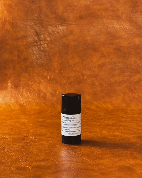 Afternoon Tea Solid Fragrance in black tube on leather background.