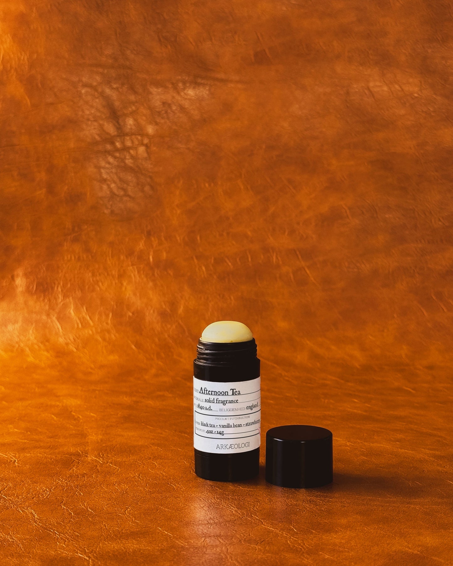 Afternoon Tea Solid Fragrance in black tube on leather background.