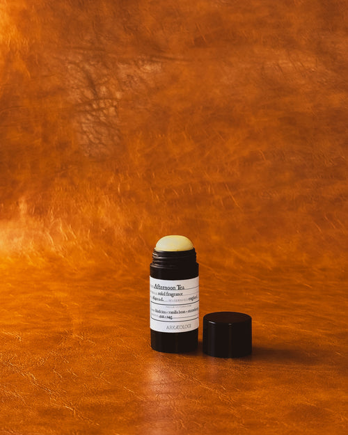 Afternoon Tea Solid Fragrance in black tube on leather background.