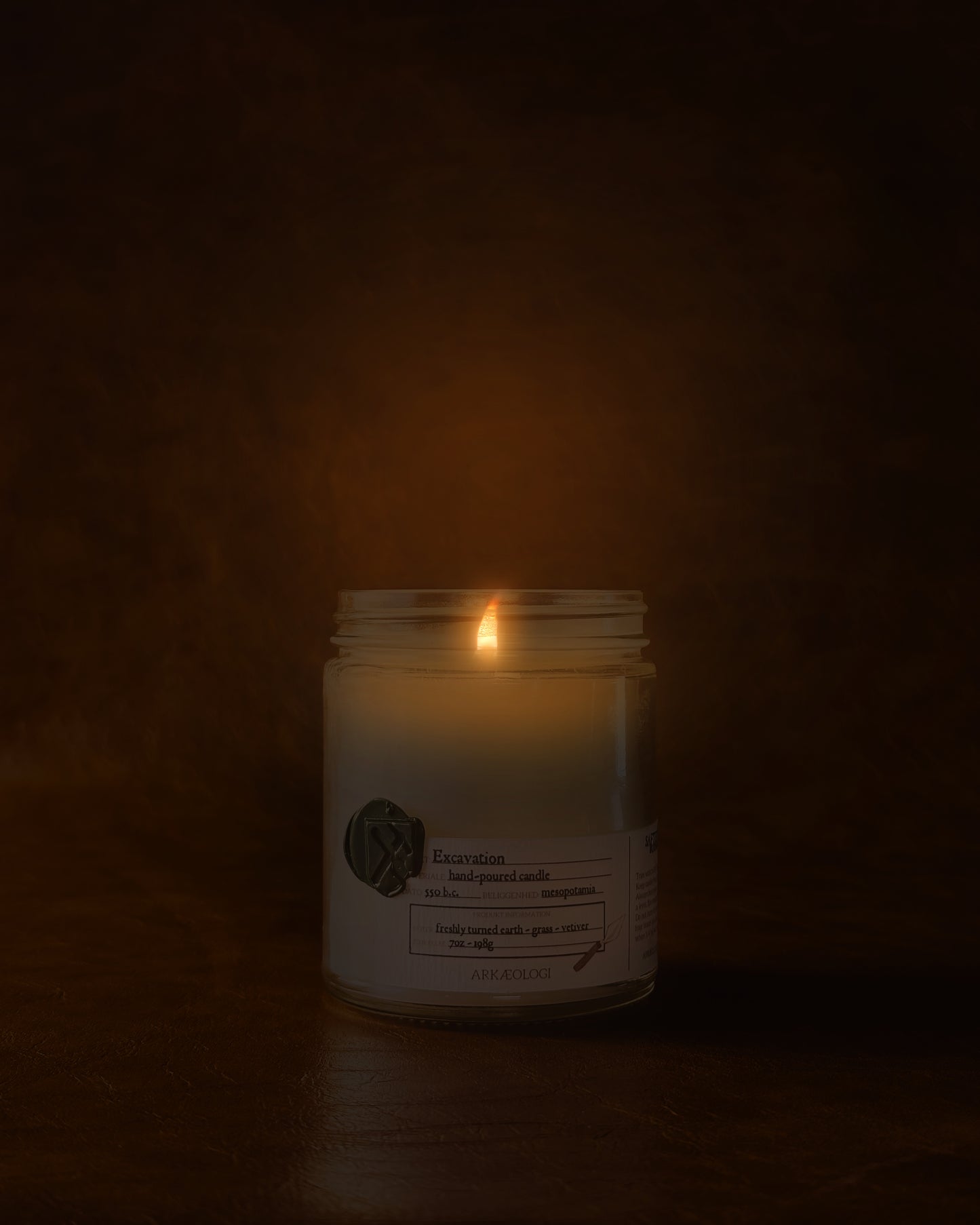 Lit Excavation in clear jar with green wax seal and white label inspired by artifact tag on leather background
