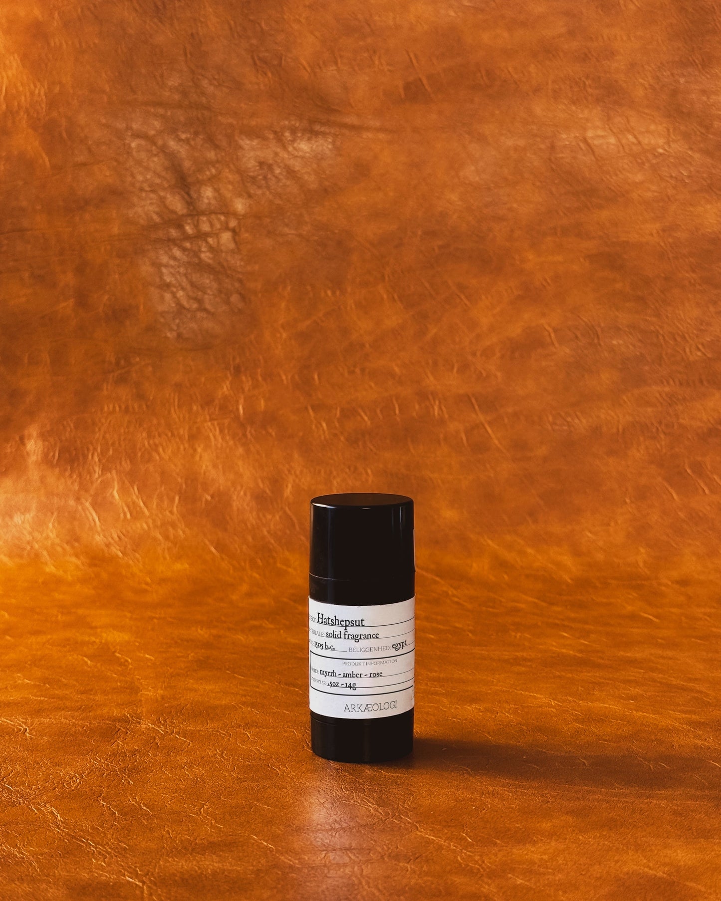 Hatshepsut Solid Fragrance in black tube on leather background.