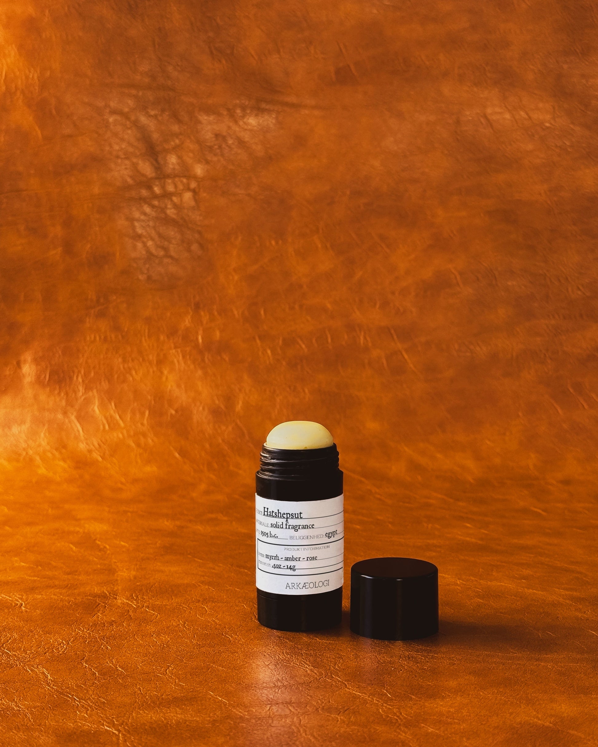 Hatshepsut Solid Fragrance in black tube on leather background.