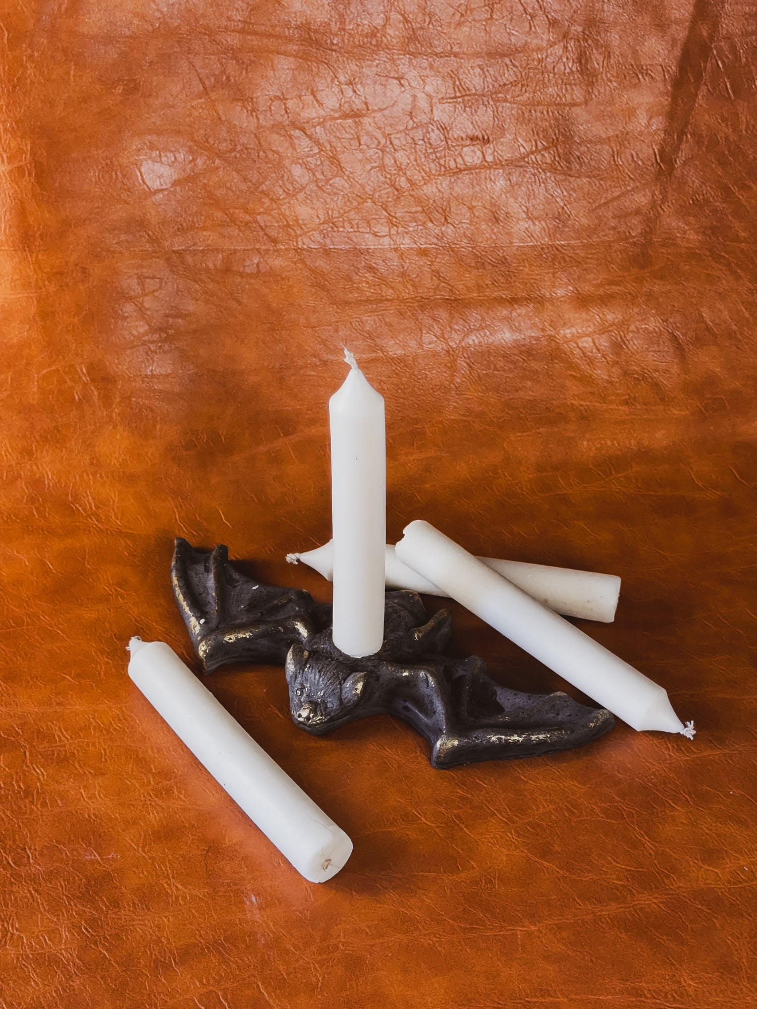 Taper candles and a Benny the Bat concrete candle holder against a brown leather background