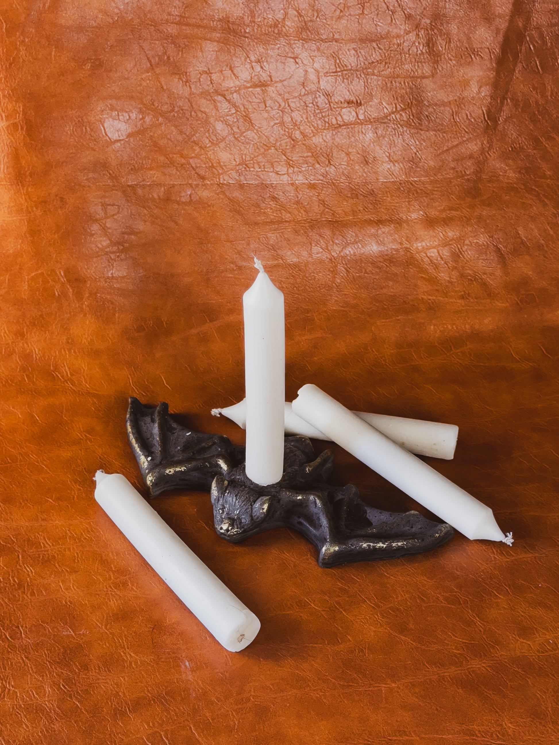 Taper candles and a Benny the Bat concrete candle holder against a brown leather background