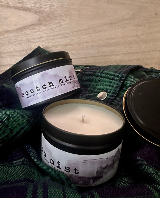 Two Black Tin Candles with Scotch Mist label on green and blue tartan with a wood background.