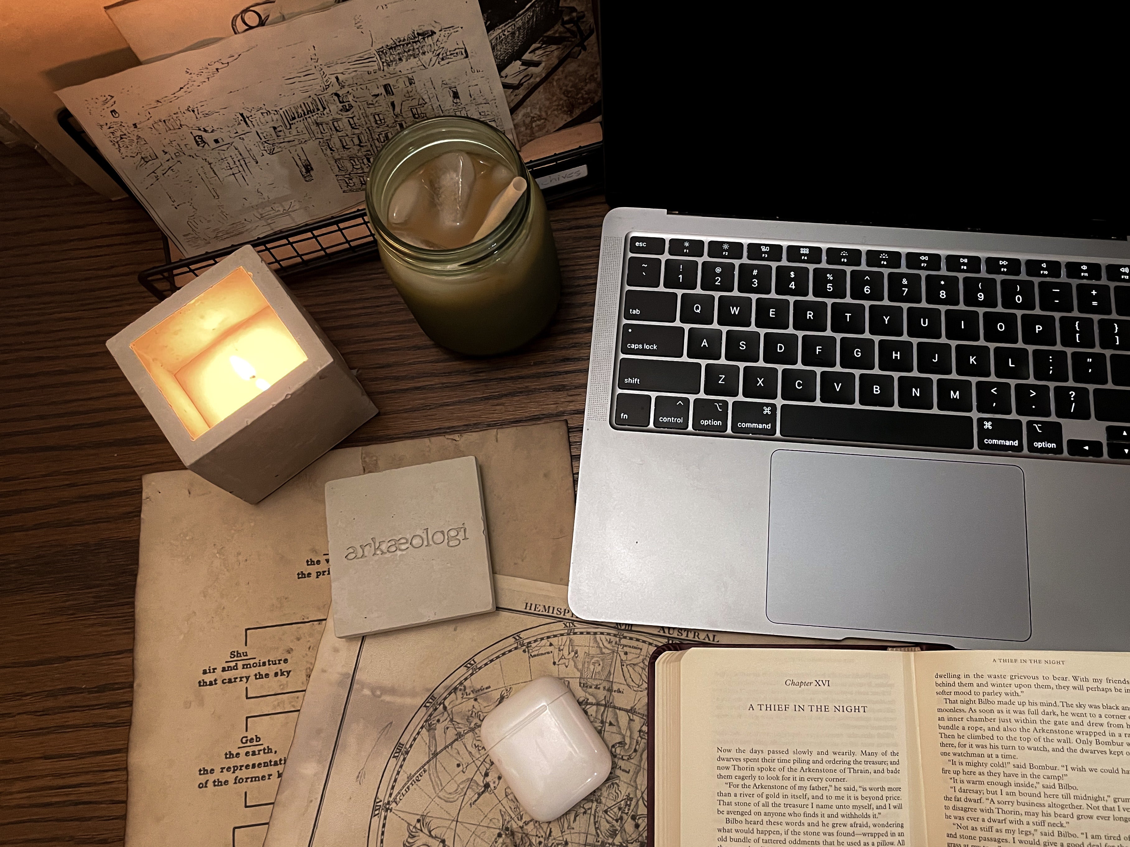 1)	A scented candle lit in a concrete jar, next to a laptop and open book, and iced coffee on a wood table.