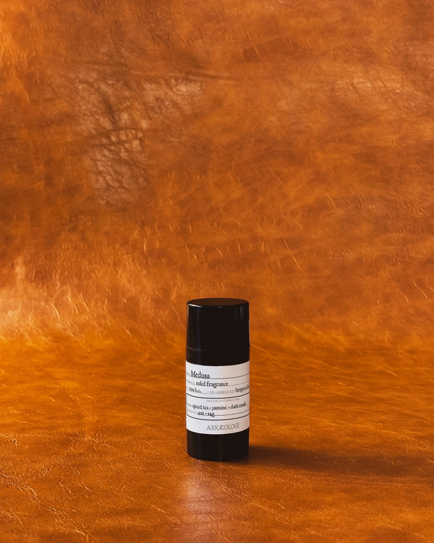 Medusa Solid Fragrance in black tube on leather background.
