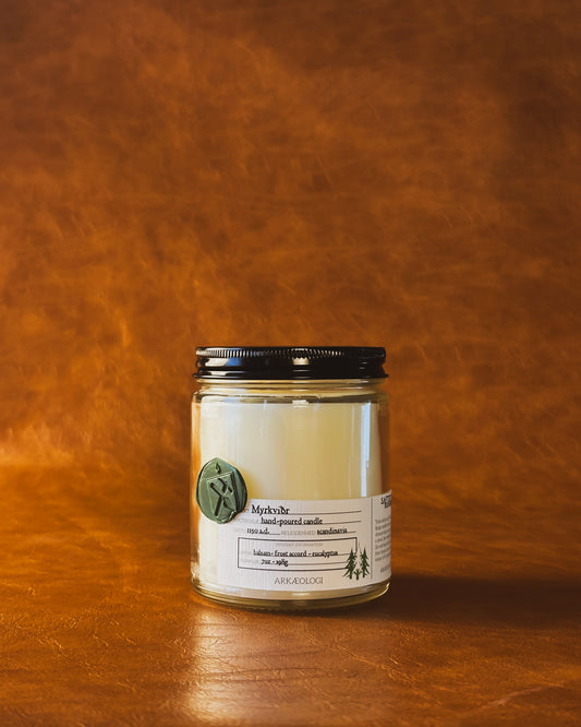 Myrkviðr candle in clear jar with green wax seal and white label inspired by artifact tag, with black lid on leather background