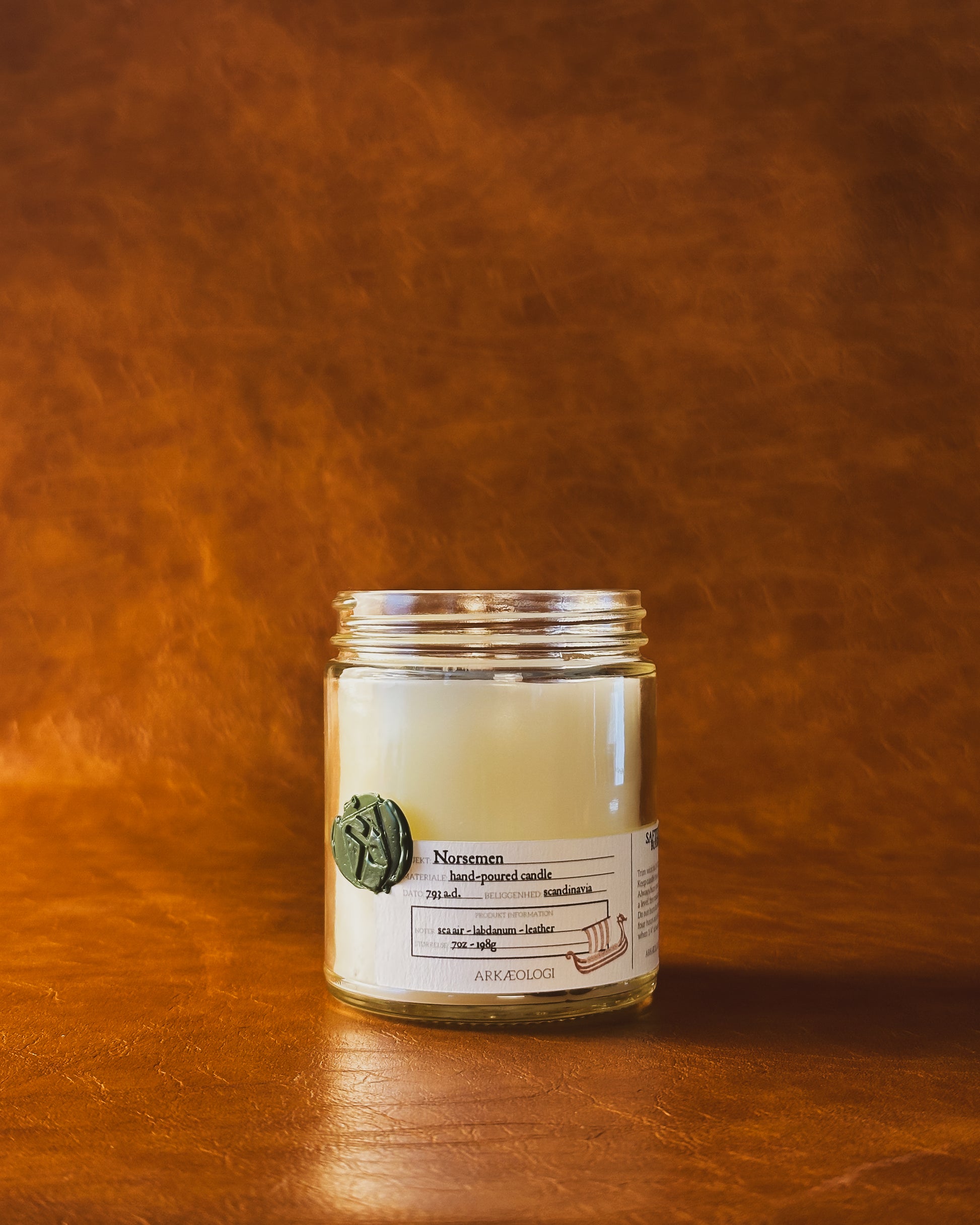 Norsemen candle jar with green wax seal and white label inspired by artifact tag, no lid on leather background