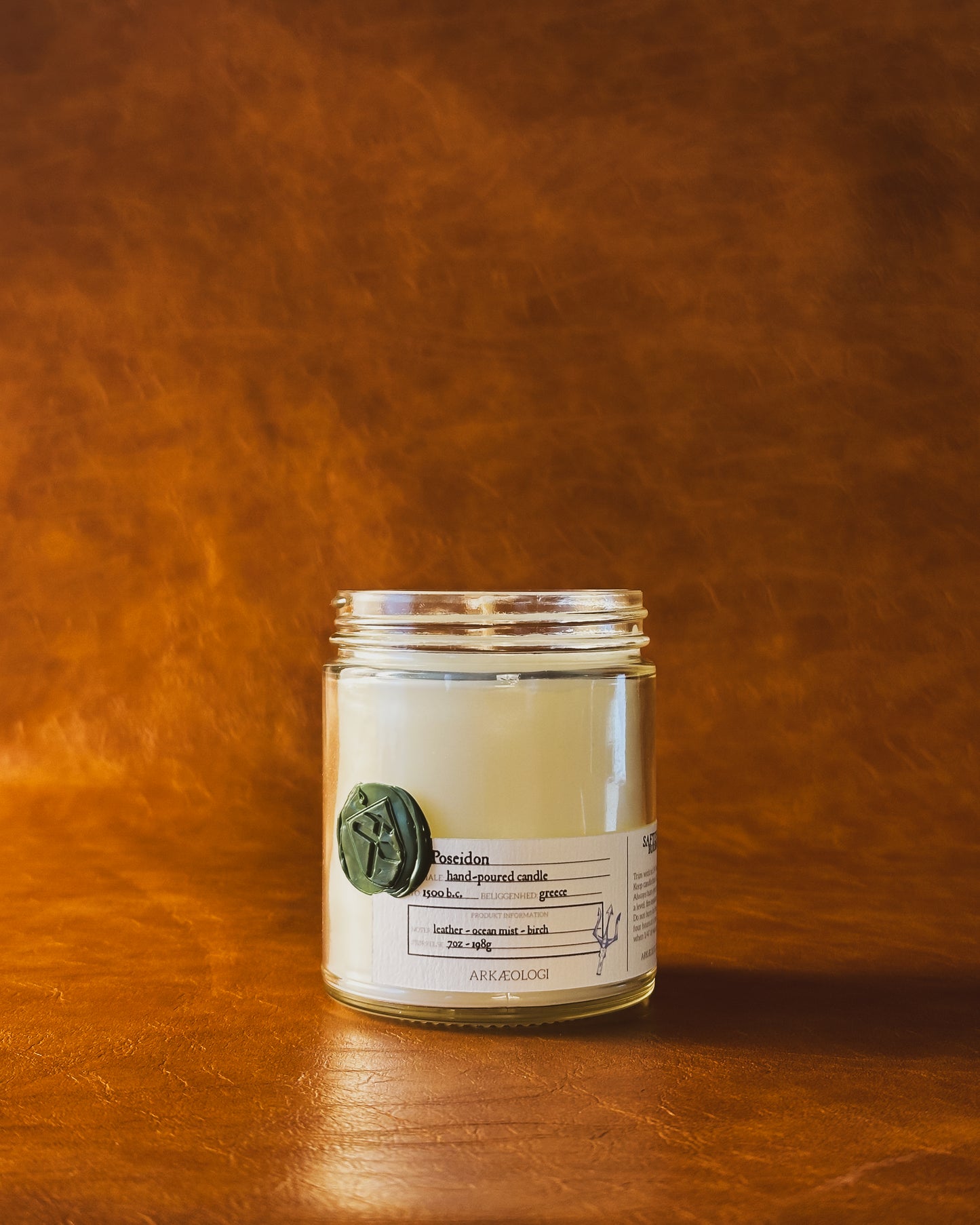 Poseidon candle jar with green wax seal and white label inspired by artifact tag, no lid on leather background