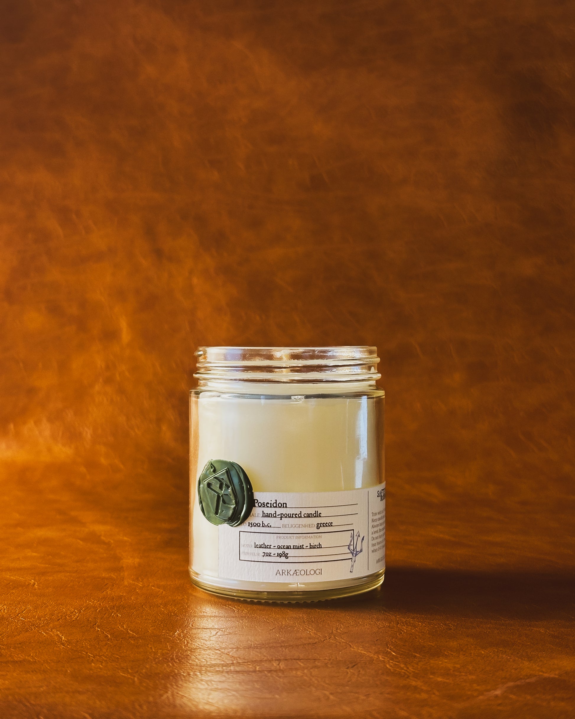 Poseidon candle jar with green wax seal and white label inspired by artifact tag, no lid on leather background