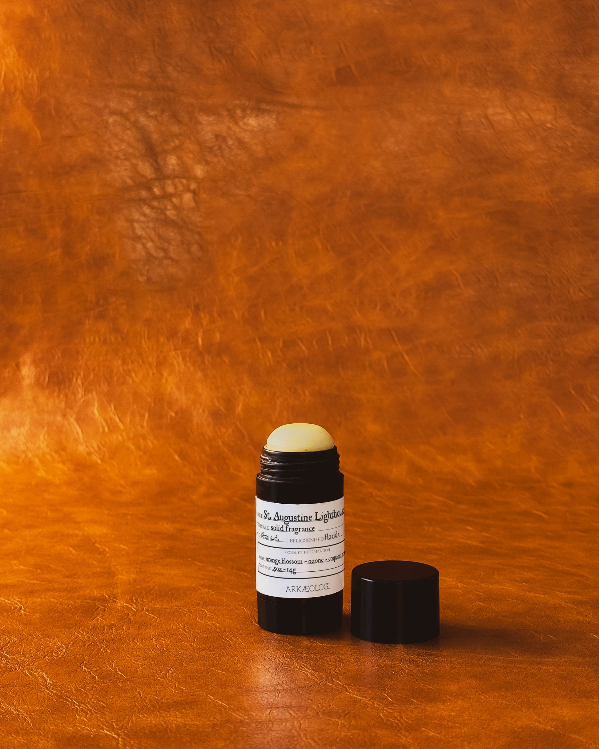 Saint Augustine Lighthouse Solid Fragrance in black tube on leather background.