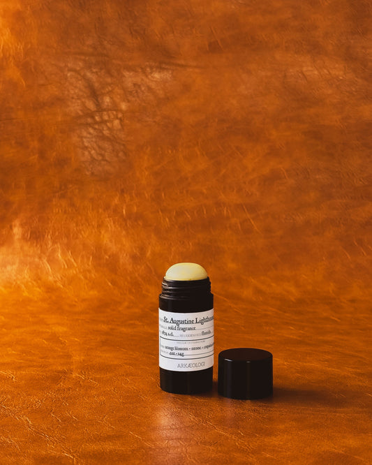 Saint Augustine Lighthouse Solid Fragrance in black tube on leather background.