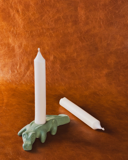 Green alligator candle holder with two taper candles on brown leather background.