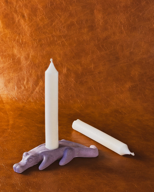 Purple alligator candle holder with two taper candles on brown leather background.