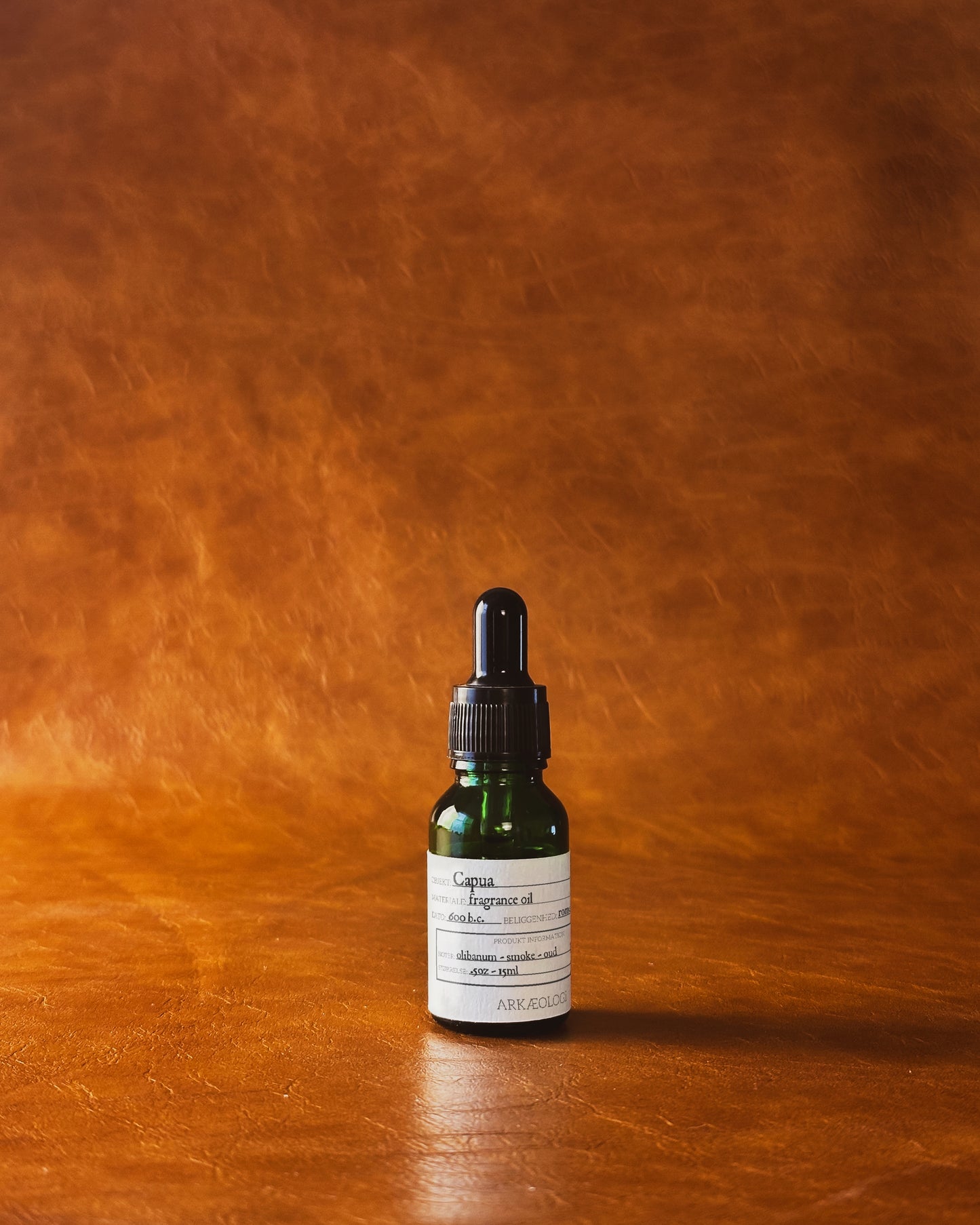 Green bottle of Capua fragrance oil on leather background.