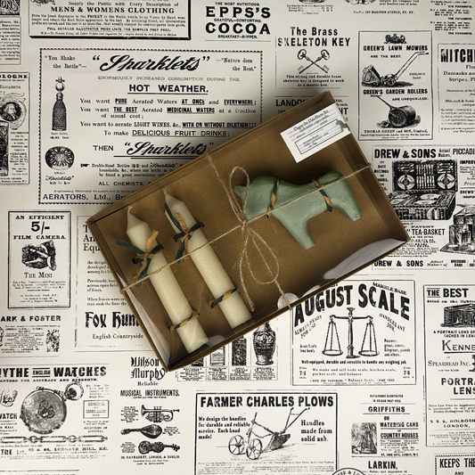 Dagny the Dala Horse box set with two taper candles and a green concrete horse candle holder on vintage newspaper background.