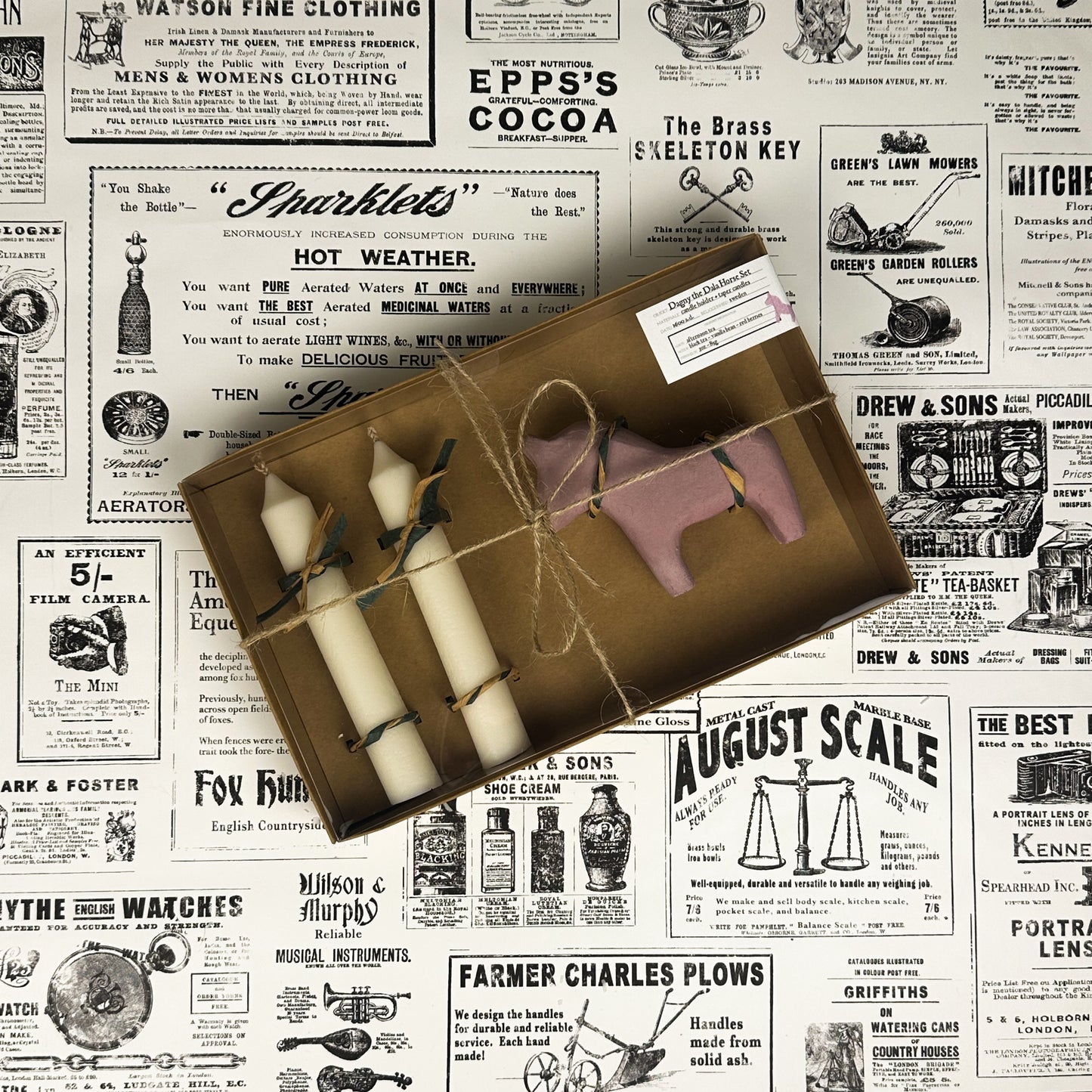 Dagny the Dala Horse box set with two taper candles and a pink concrete horse candle holder on vintage newspaper background.