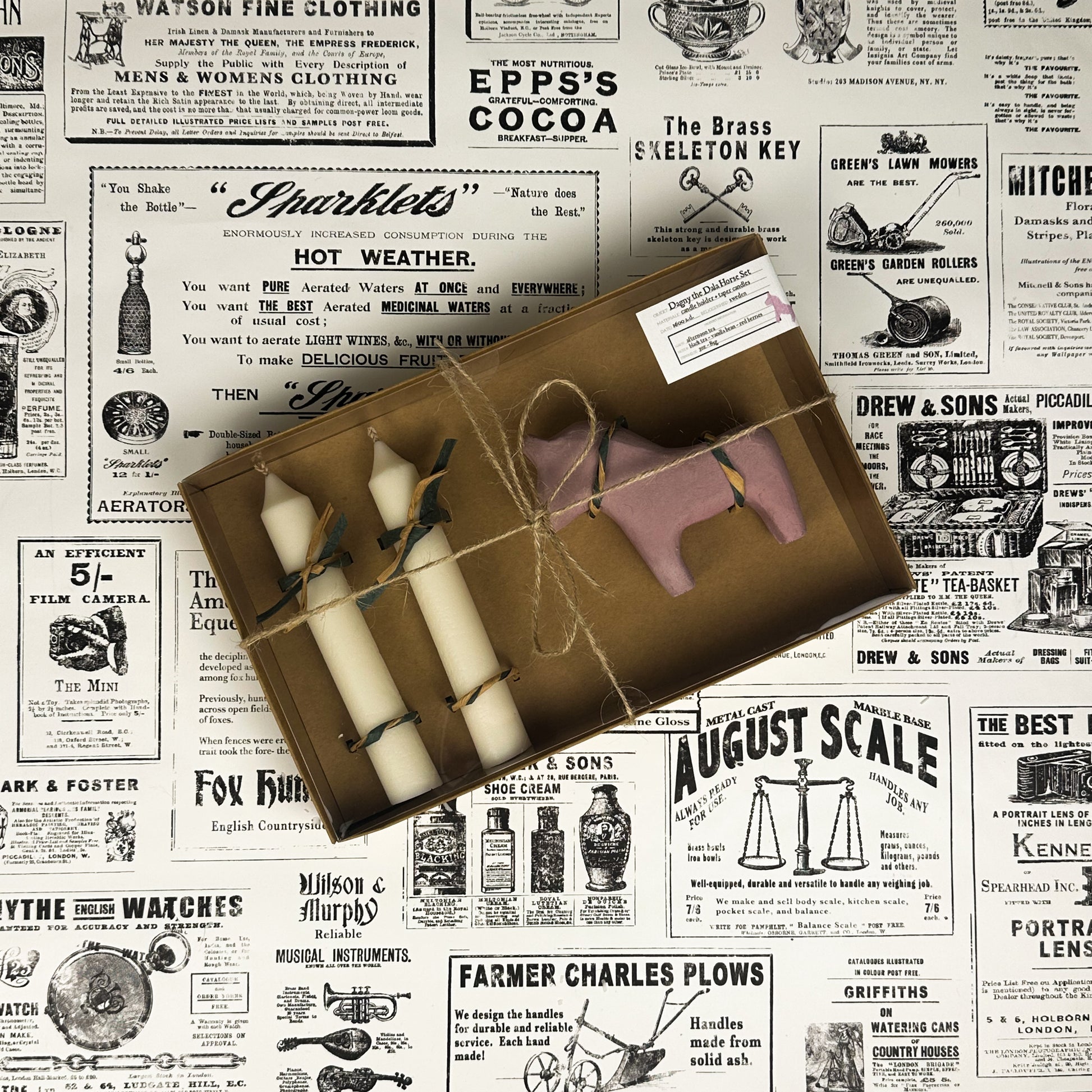 Dagny the Dala Horse box set with two taper candles and a pink concrete horse candle holder on vintage newspaper background.