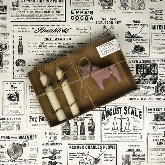 Dagny the Dala Horse box set with two taper candles and a pink concrete horse candle holder on vintage newspaper background.