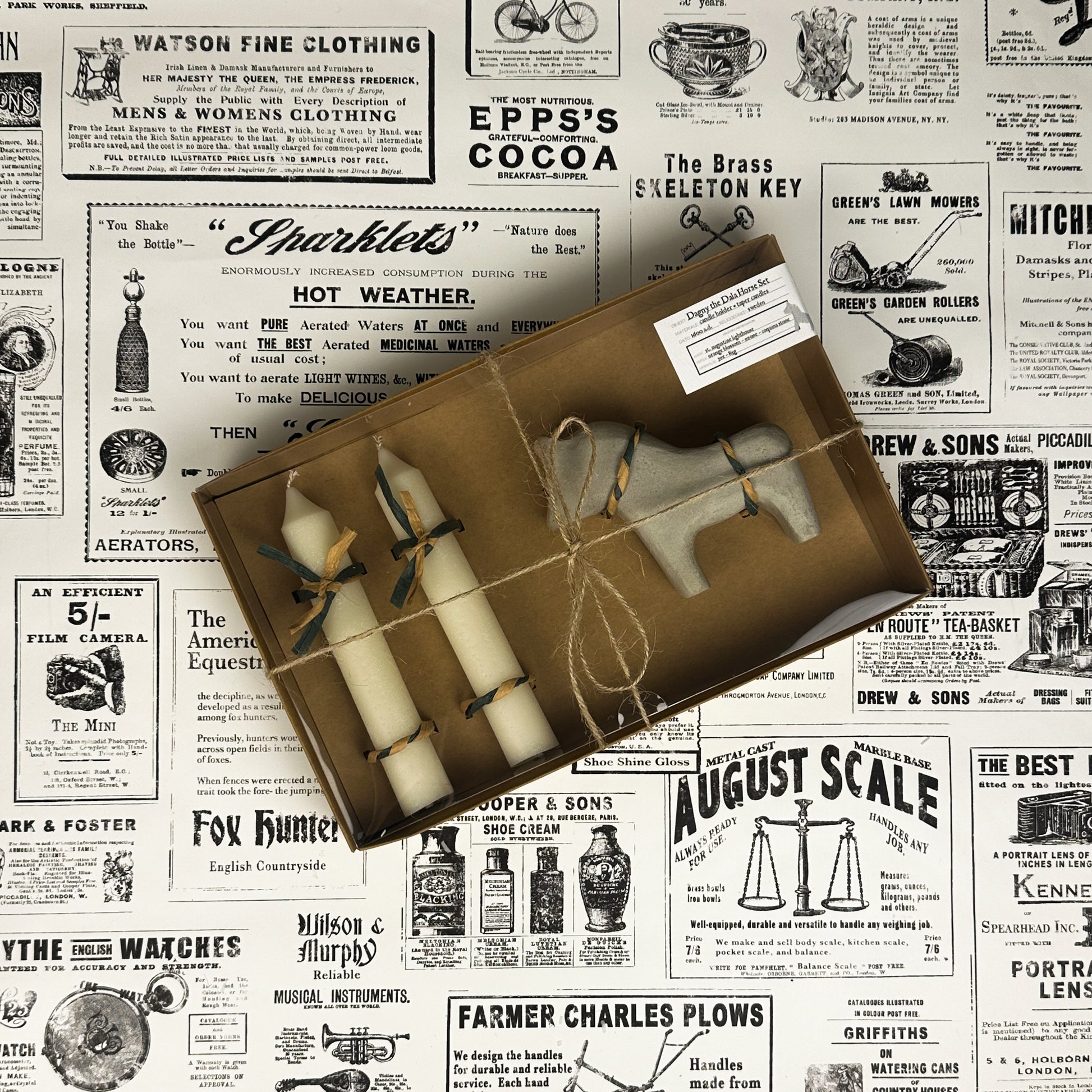 Dagny the Dala Horse box set with two taper candles and a white concrete horse candle holder on vintage newspaper background.