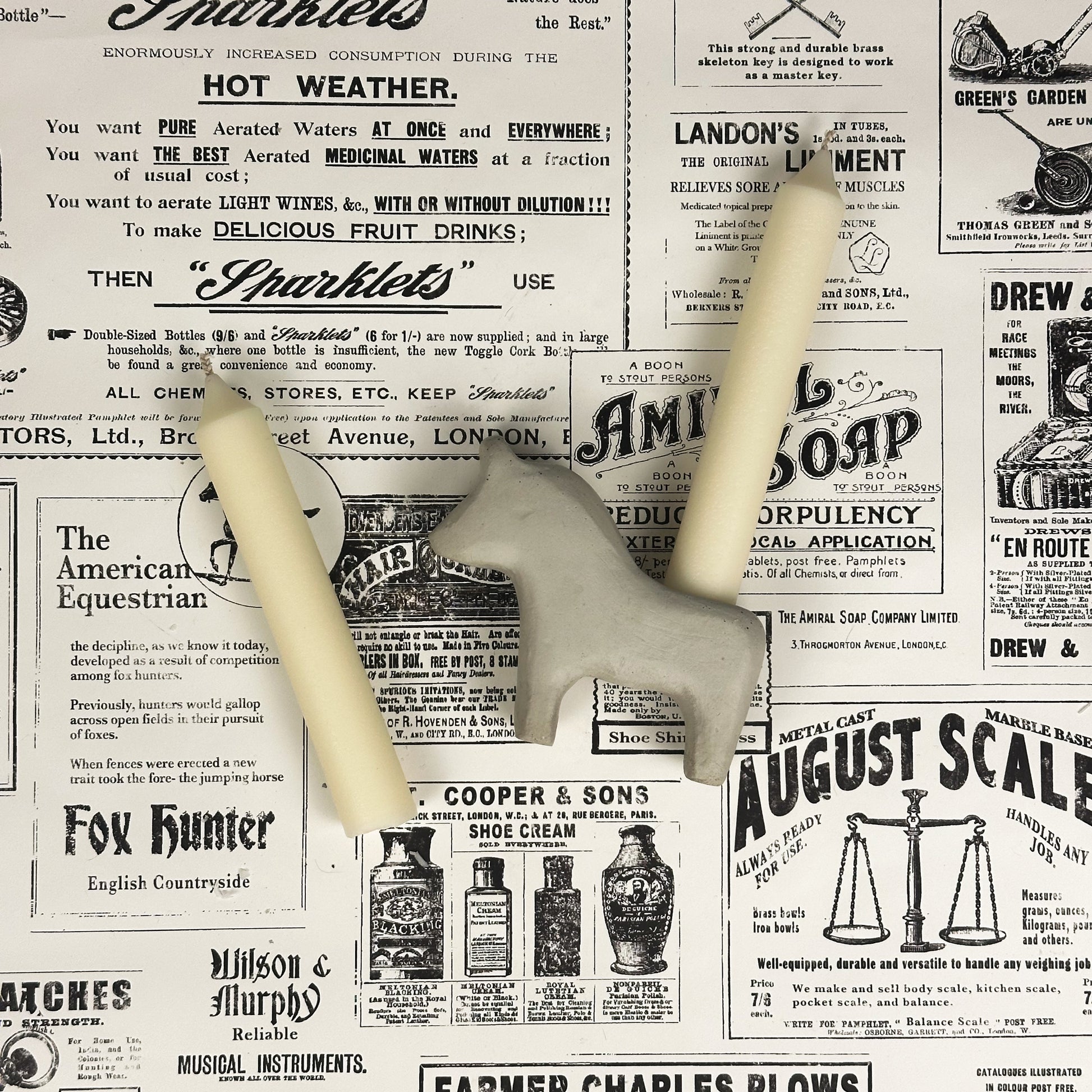 White concrete Dala horse candle holder with two taper candles on vintage newspaper background.