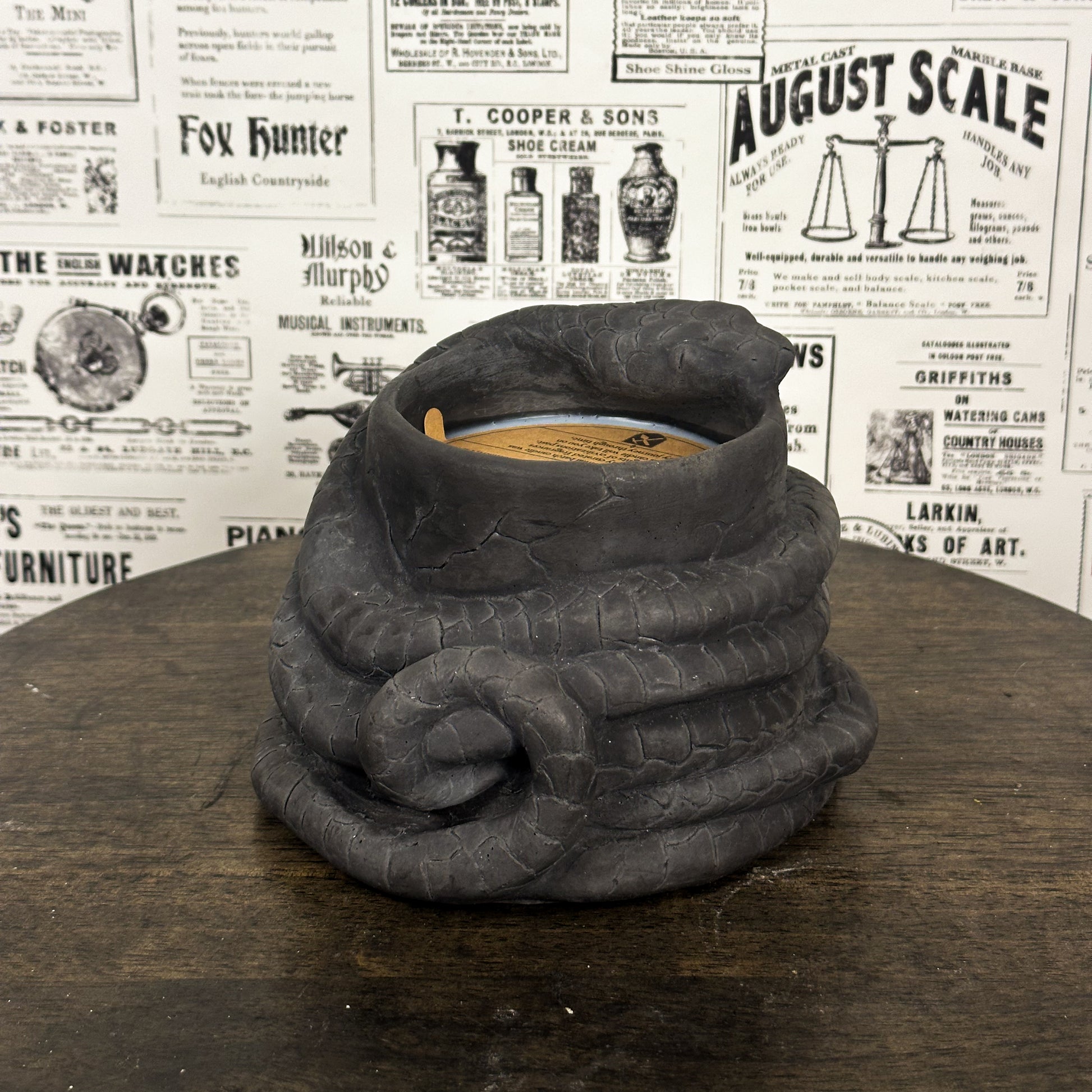 Black Concrete Medusa Snake candle on wooden table with vintage newspaper background.