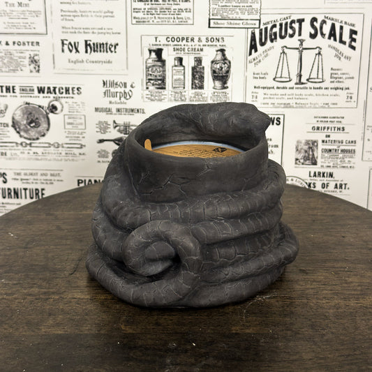 Black Concrete Medusa Snake candle on wooden table with vintage newspaper background.