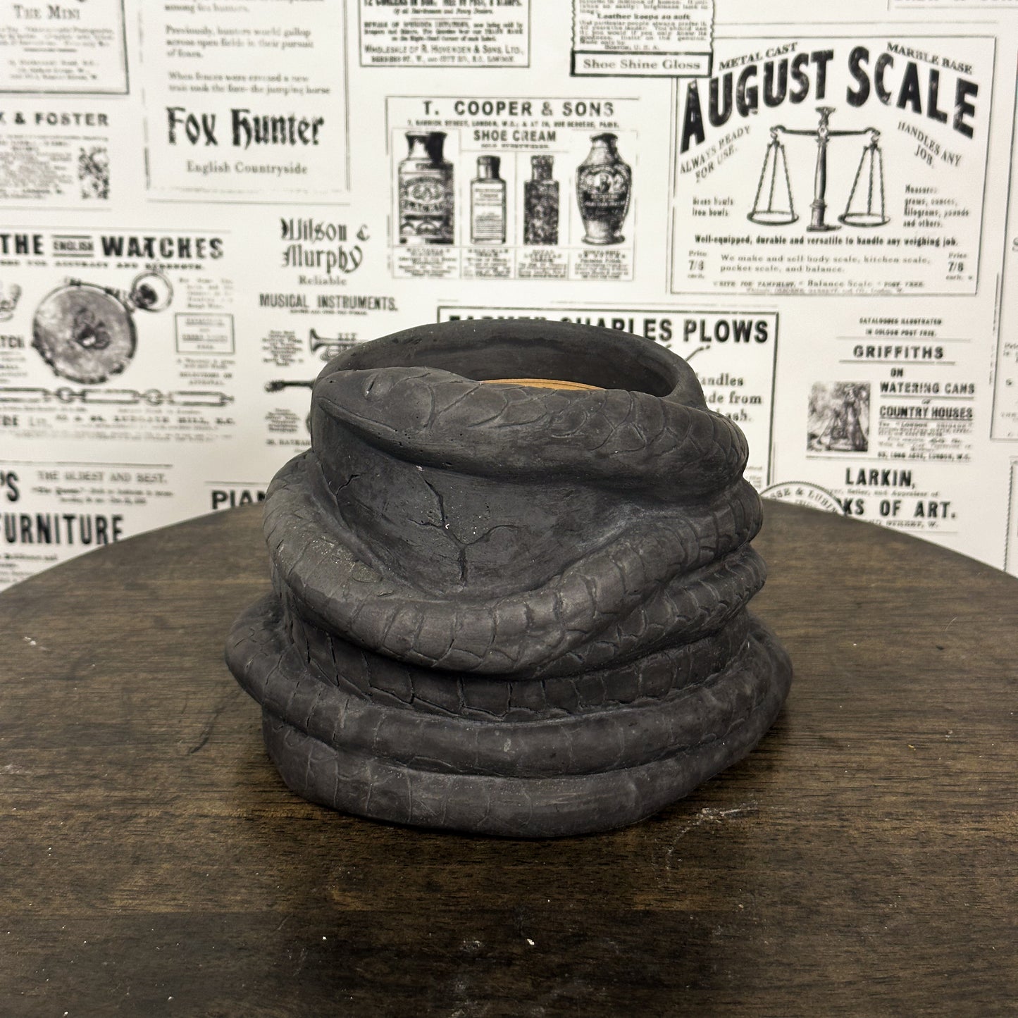 Black Concrete Medusa Snake candle on wooden table with vintage newspaper background.