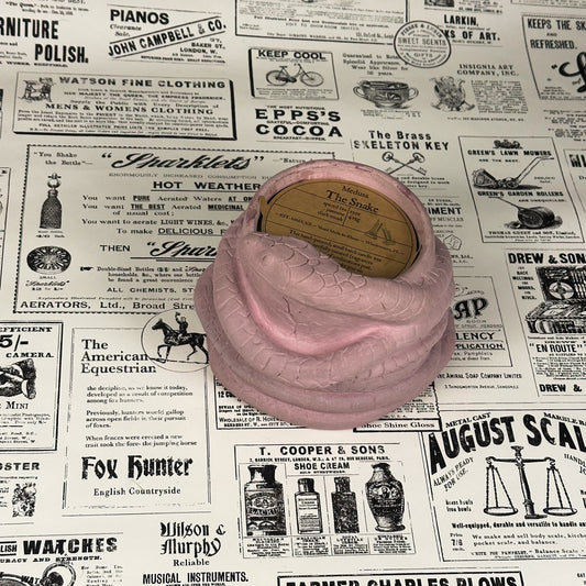 Pink Concrete Medusa Snake candle with brown insert and reads "The Snake" on vintage newspaper background.