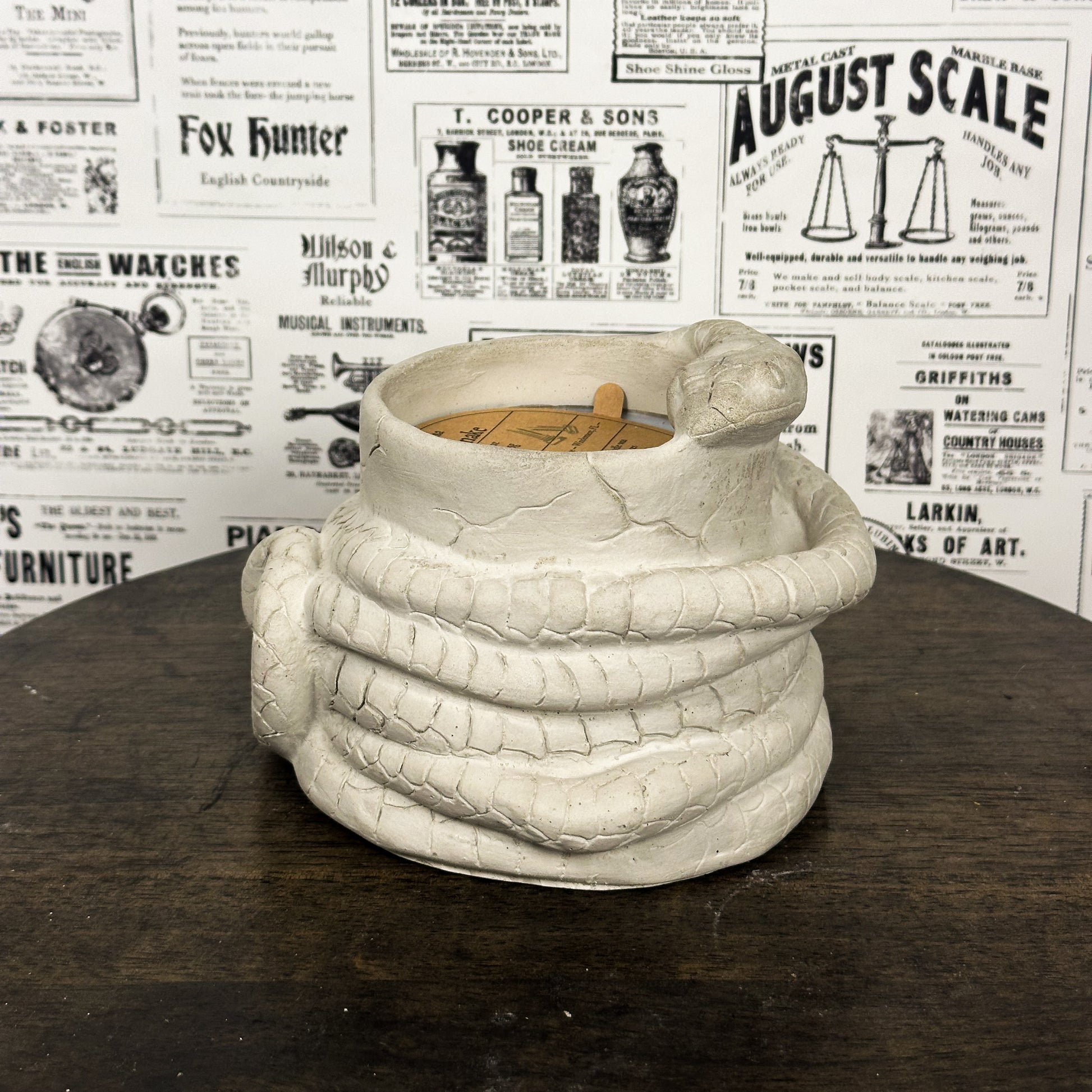 White Concrete Medusa Snake candle on wooden table with vintage newspaper background.
