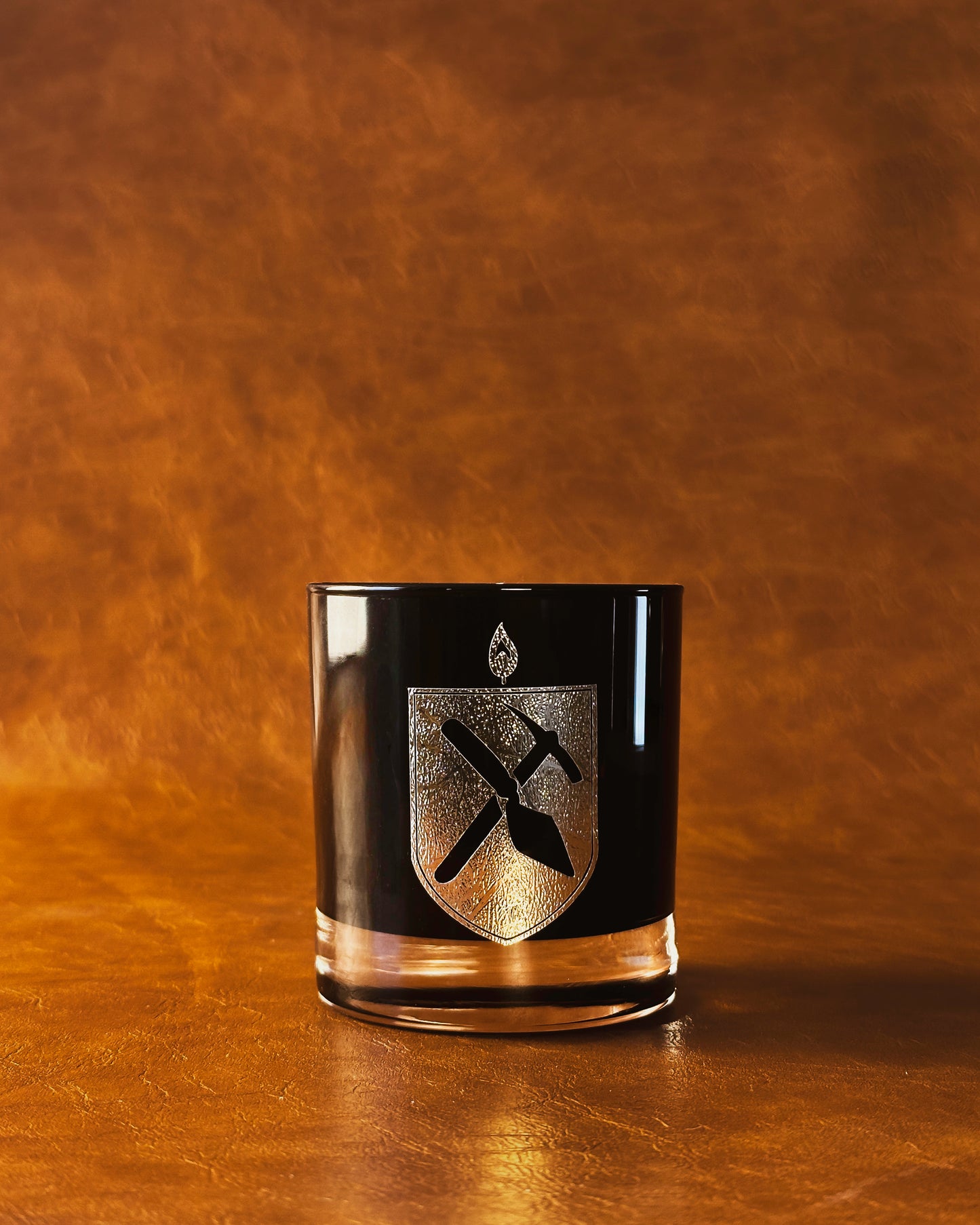 Black Glass Candle with gold Arkæologi crest on orange leather background 