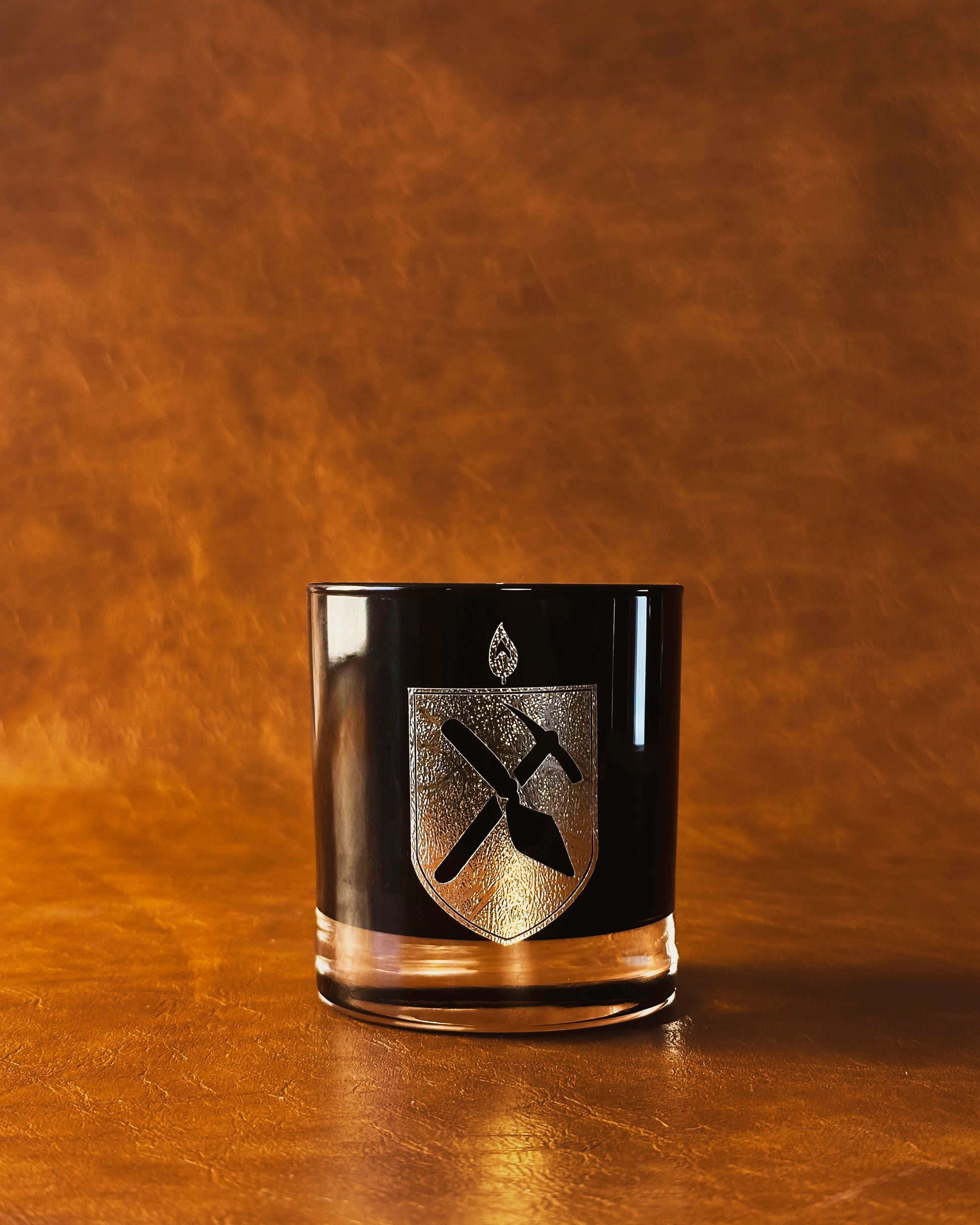 Black Glass Candle with gold Arkæologi crest on orange leather background 