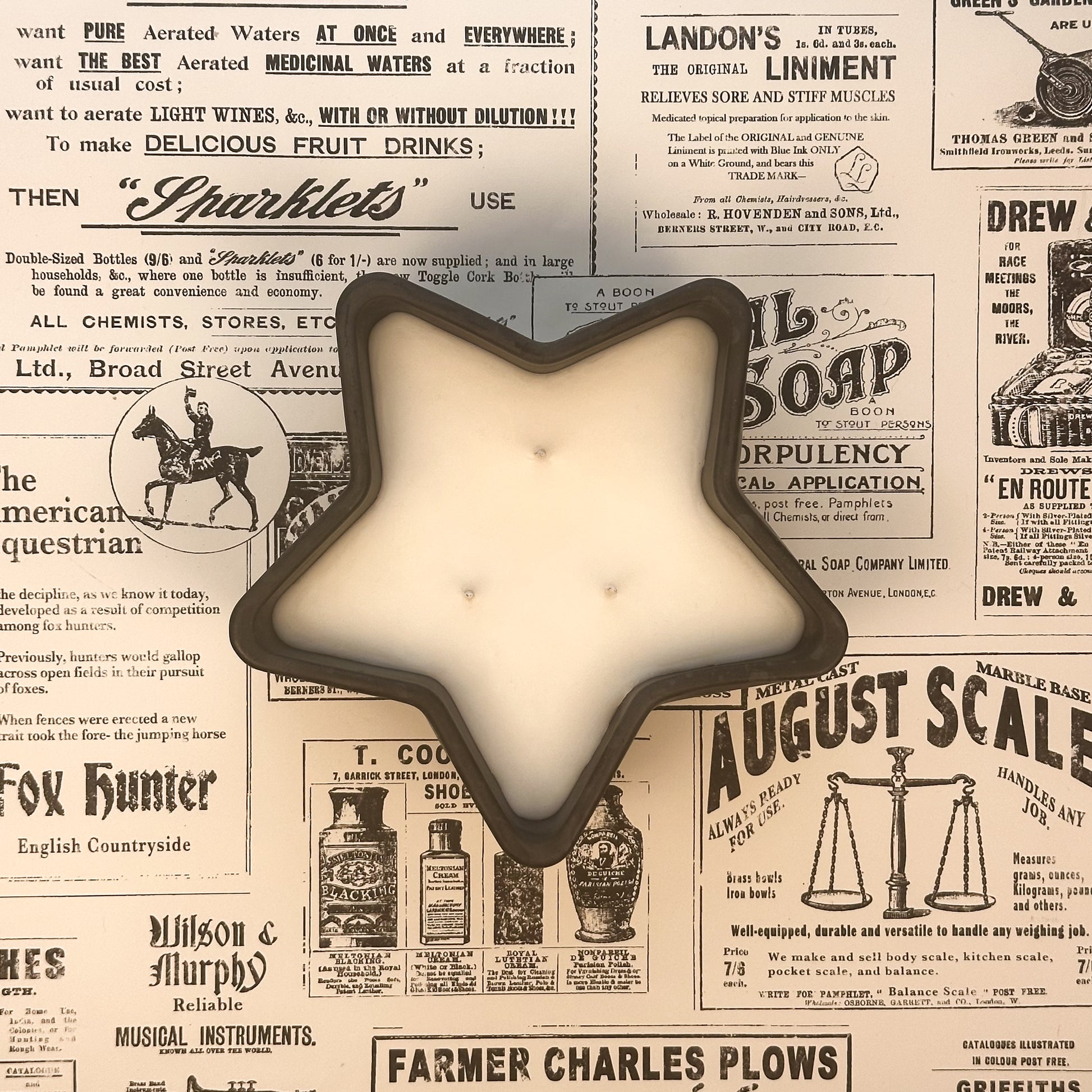 Black concrete star shaped three wick candle on an old newspaper background.